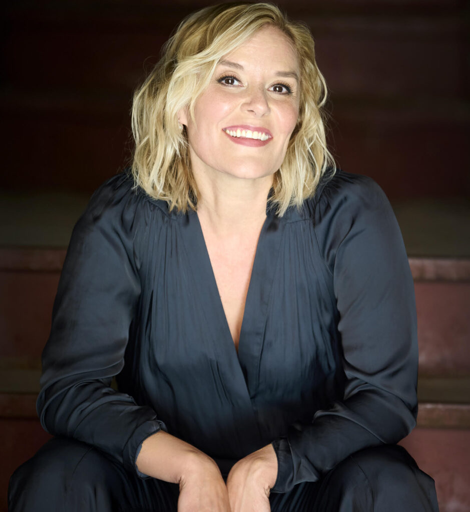 Portrait souriant de Rachelle Elie, humoriste reconnue et animatrice des spectacles d’humour à La Ferme Kerr, vêtue d'un élégant chemisier foncé.